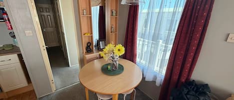 A compact living space with a round wooden dining table, a kitchenette, a sofa, and a window with curtains.