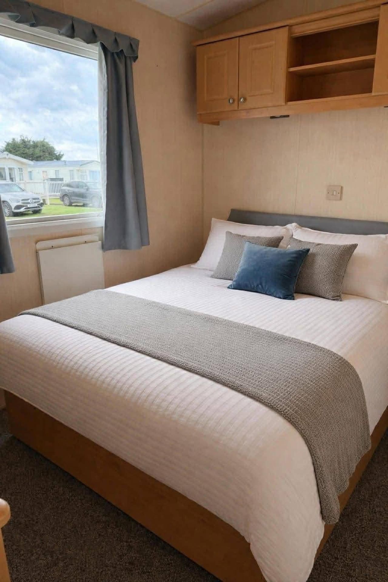 Quarto com cama, janela com cortinas, armário de madeira sobre a cama e vista para o exterior.