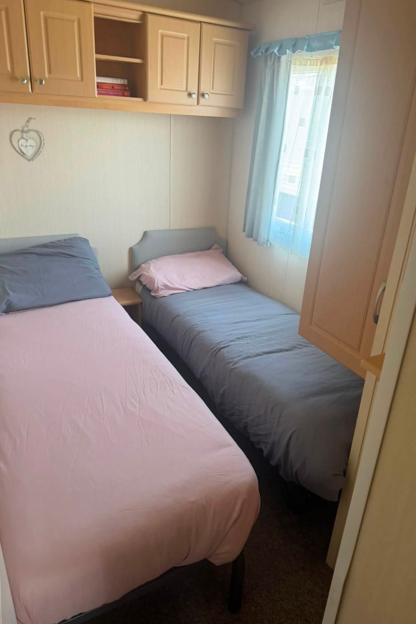 A bedroom with two single beds, a wardrobe, and a window with curtains.