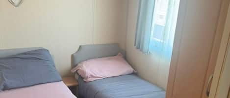 A bedroom with two single beds, a wardrobe, and a window with curtains.