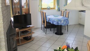 En stue med tv, spisebord, stole og et køkkenområde.
