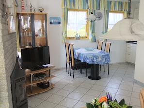 Ein Wohnzimmer mit Fernseher, Esstisch, Stühlen und einer Küchenzeile.