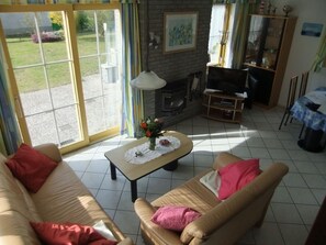 A living room with a sofa, armchair, TV, fireplace, and a view of the garden through large windows. - A lovely vacation home where the whole family can relax and unwind on the coast (Julianadorp)