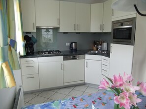 A kitchen with white cabinets, a gas stove, a microwave, and a sink. - A lovely vacation home where the whole family can relax and unwind on the coast (Julianadorp)