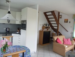 Ein kompakter Wohnraum mit Küchenzeile, Essbereich inklusive Tisch und Stühlen, einer Couch, einer Treppe und einem kleinen Bücherregal.