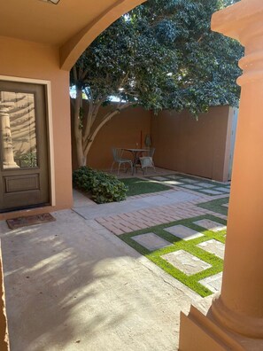 Eine Terrasse mit Tisch, Stühlen, einer Tür und einem kleinen Gartenbereich.