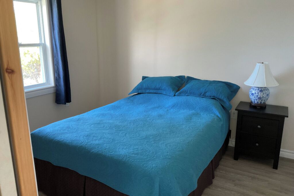 Une chambre à coucher avec un lit, une table de chevet, une lampe et une fenêtre avec des rideaux.