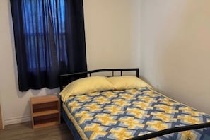 Ein Einzelbett mit einem gemusterten Bettbezug, ein Nachttisch und ein Fenster mit dunklen Vorhängen.