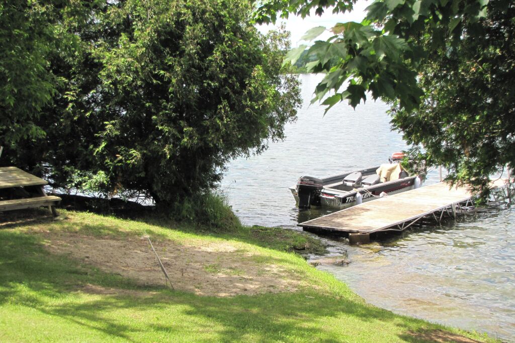 Une jetée avec un bateau, une table de pique-nique et une zone herbeuse au bord d’un lac paisible.