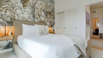 A bedroom with a large bed, white bedding, a headboard with a floral mural, two bedside lamps, and a white wardrobe.