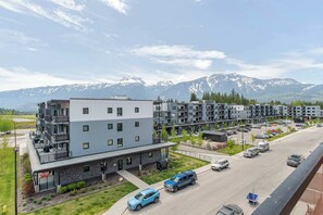 En flervåningsbyggnad med balkonger, en parkeringsplats och utsikt över snöklädda berg.
