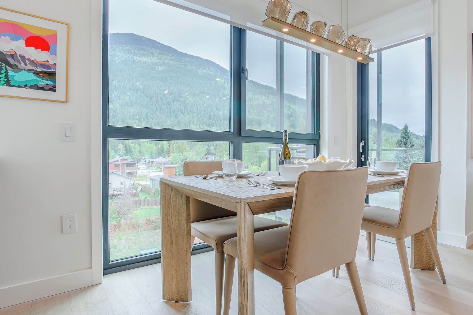 A dining area with a table set for four, large windows offering a mountain view, and a framed artwork on the wall.