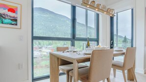 Ein Essbereich mit Tisch für vier Personen, großen Fenstern mit Bergblick und einem gerahmten Kunstwerk an der Wand.