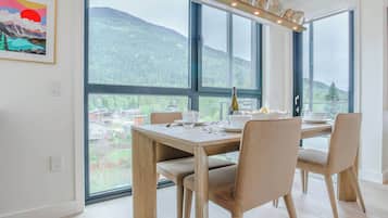 A dining area with a table set for four, large windows offering a mountain view, and a framed artwork on the wall.