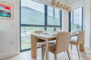 Ein Essbereich mit Tisch für vier Personen, großen Fenstern mit Bergblick und einem gerahmten Kunstwerk an der Wand.