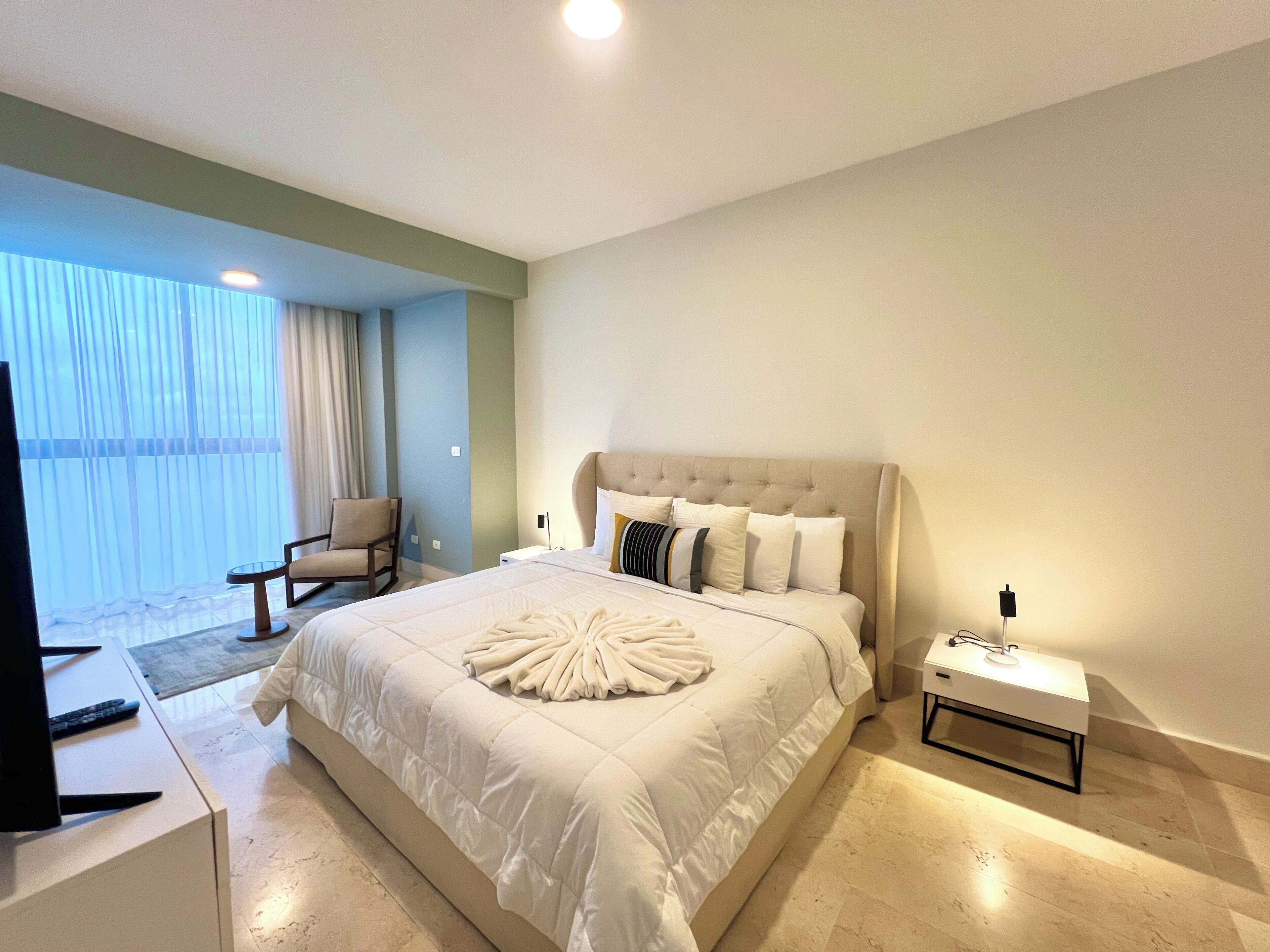 Une chambre à coucher avec un grand lit, une chaise, un téléviseur et une table de chevet avec une lampe.