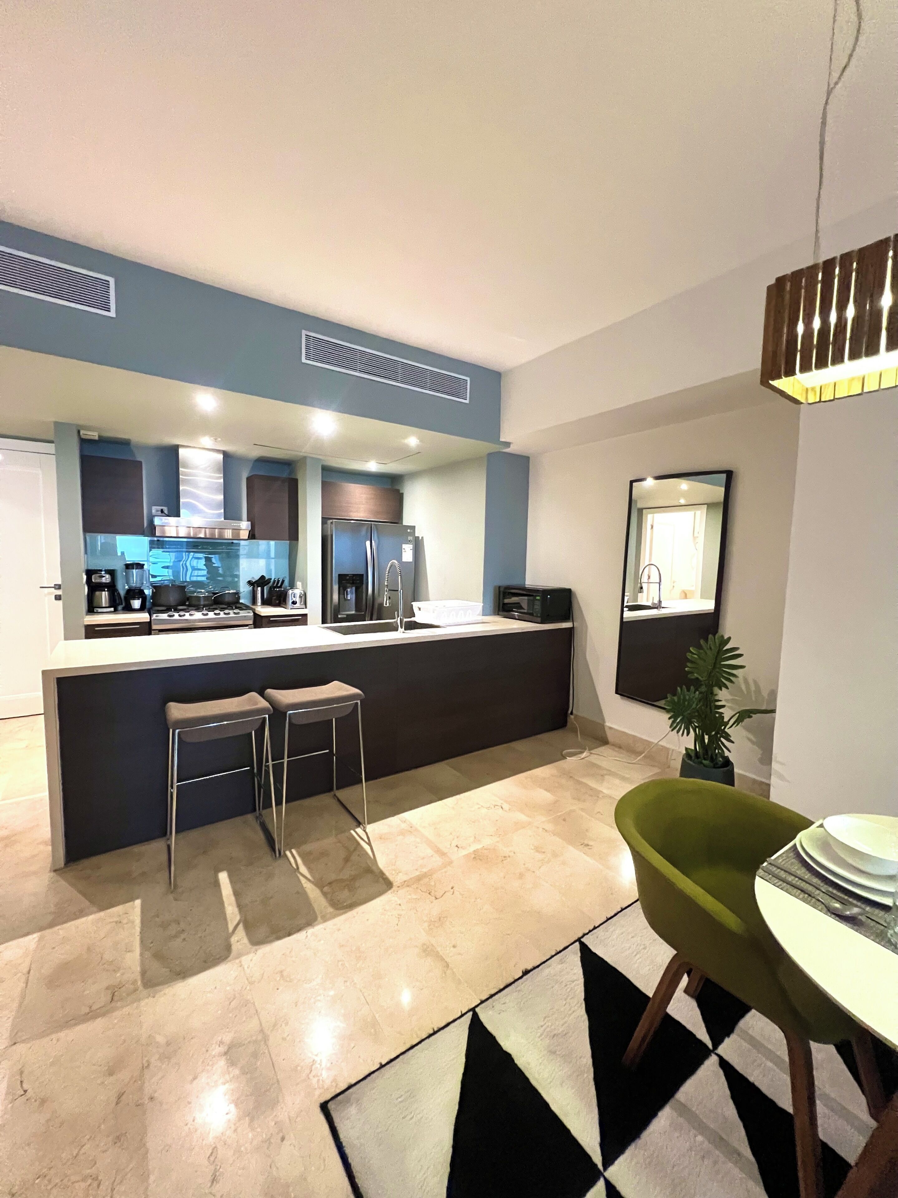 Una cocina moderna con una isla central, taburetes de bar, una silla verde y una mesa de comedor.