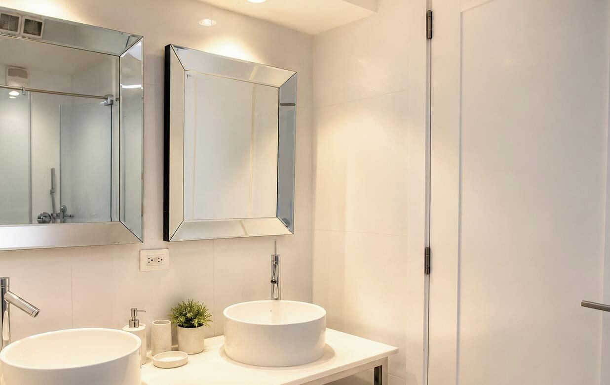 A modern bathroom with two sinks, a large mirror, and a door.