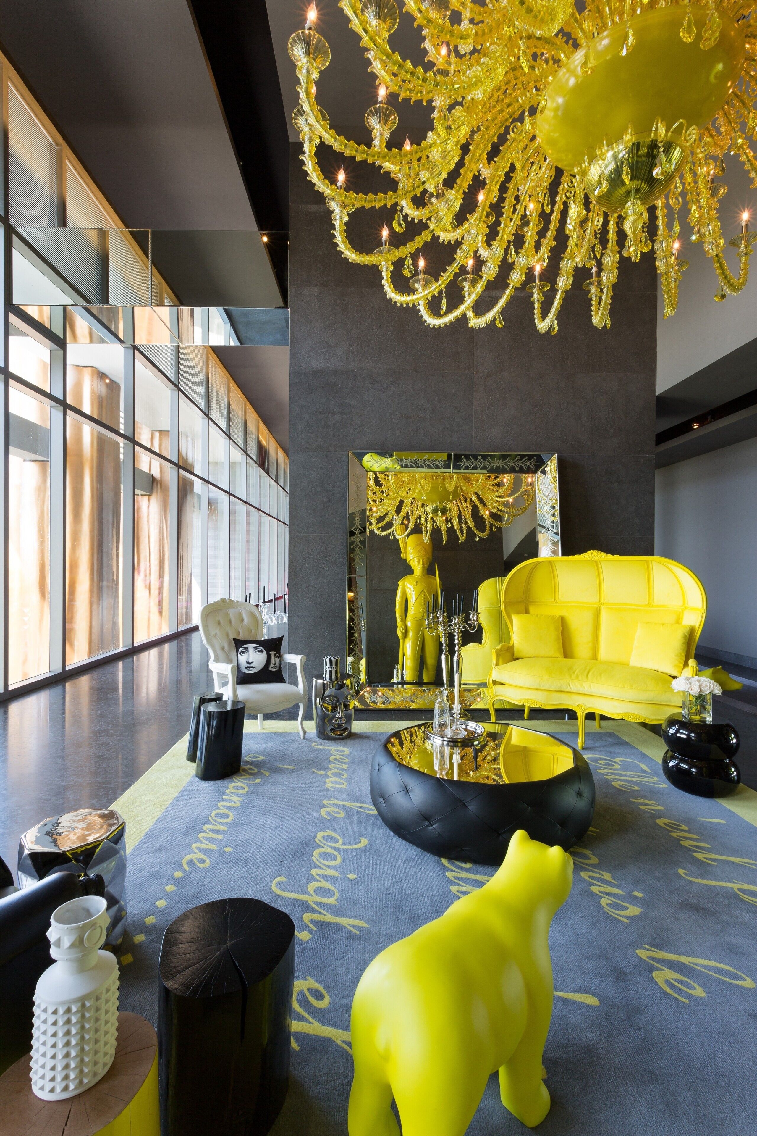 A modern interior with a yellow sofa, a reflective sculpture, and a chandelier.