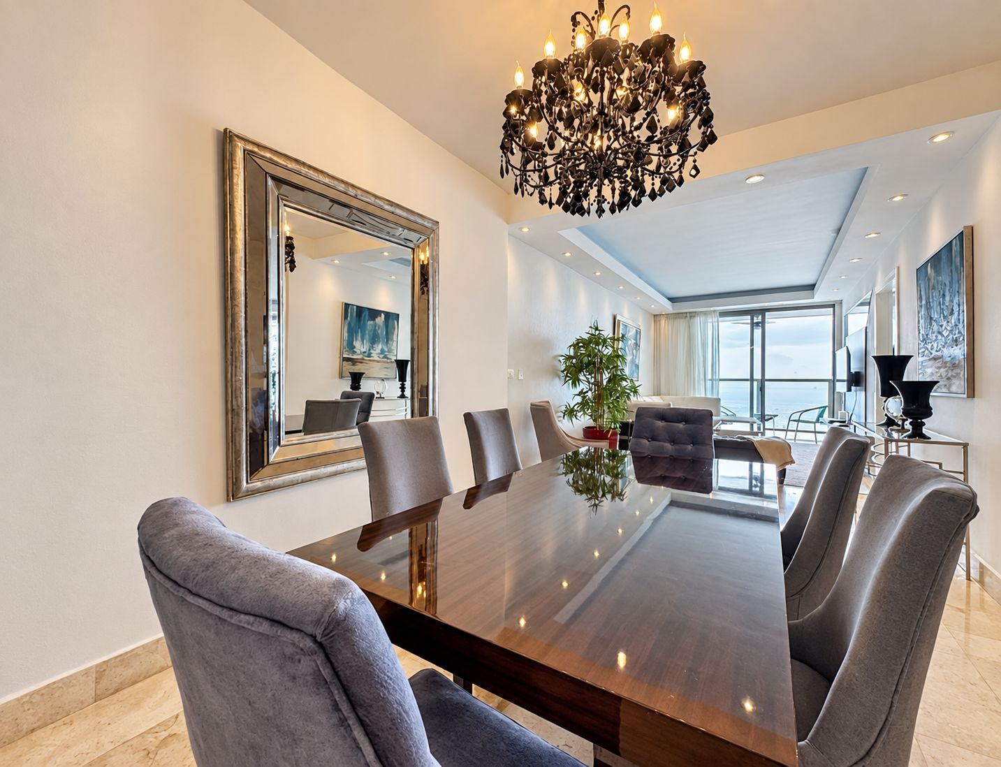 A modern dining area with a large table, chairs, a chandelier, and a large mirror on the wall.