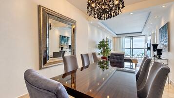 A modern dining area with a large table, chairs, a chandelier, and a large mirror on the wall.