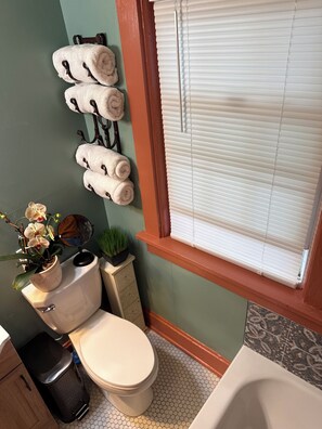Un baño con inodoro, lavabo, espejo, una planta en maceta y una ventana con persianas.