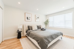 Une chambre moderne avec un grand lit, une petite table de chevet, une plante en pot et deux tableaux encadrés accrochés au mur.