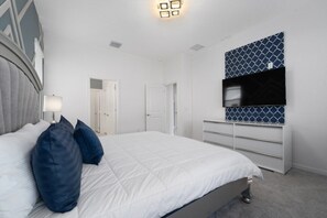 Ein Schlafzimmer mit Bett, Kissen, einem Schminktisch, einem Fernseher und einer Tür.