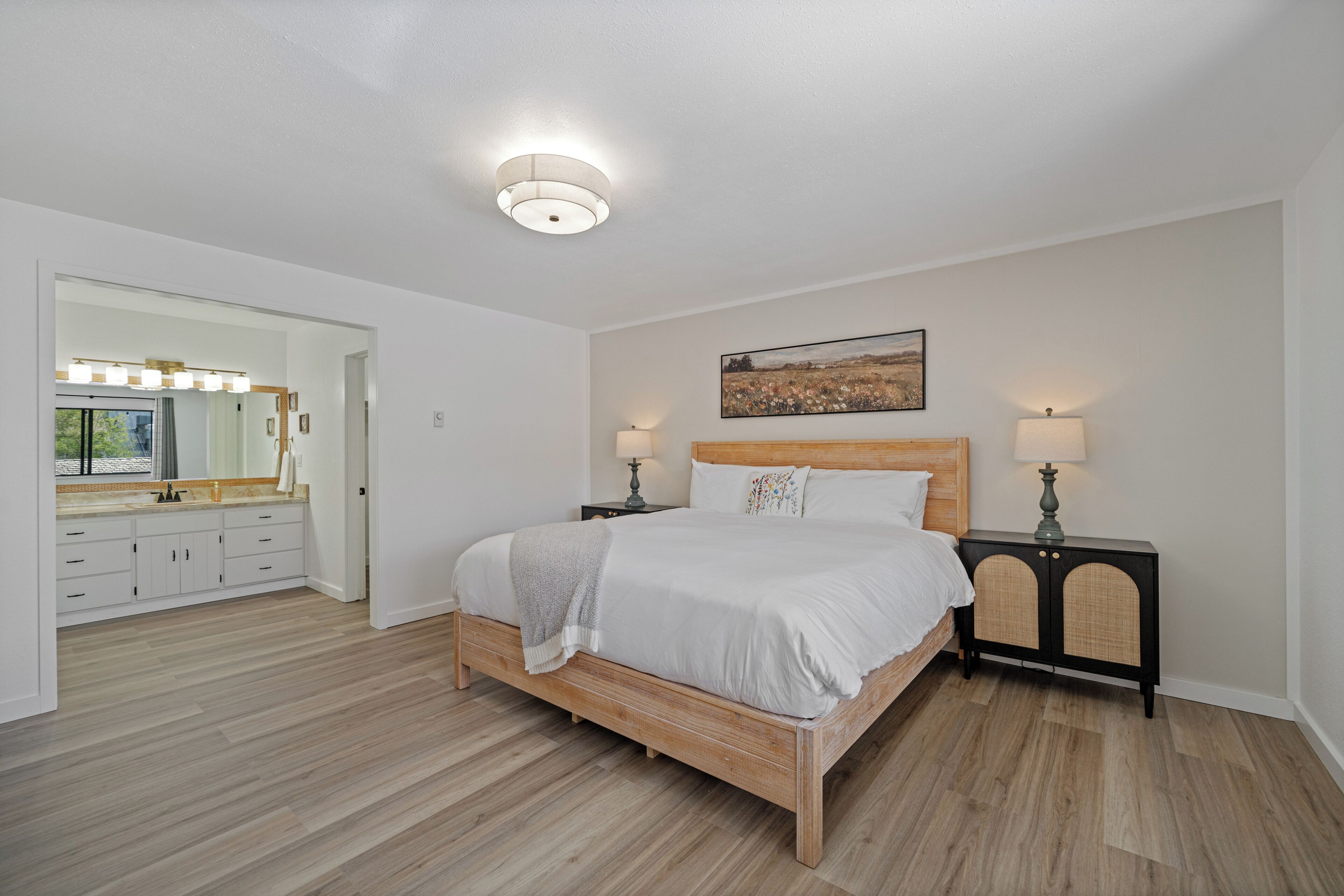 Une chambre à coucher avec un lit en bois, des lampes de chevet, une table de nuit, un miroir et un tableau accroché au mur.