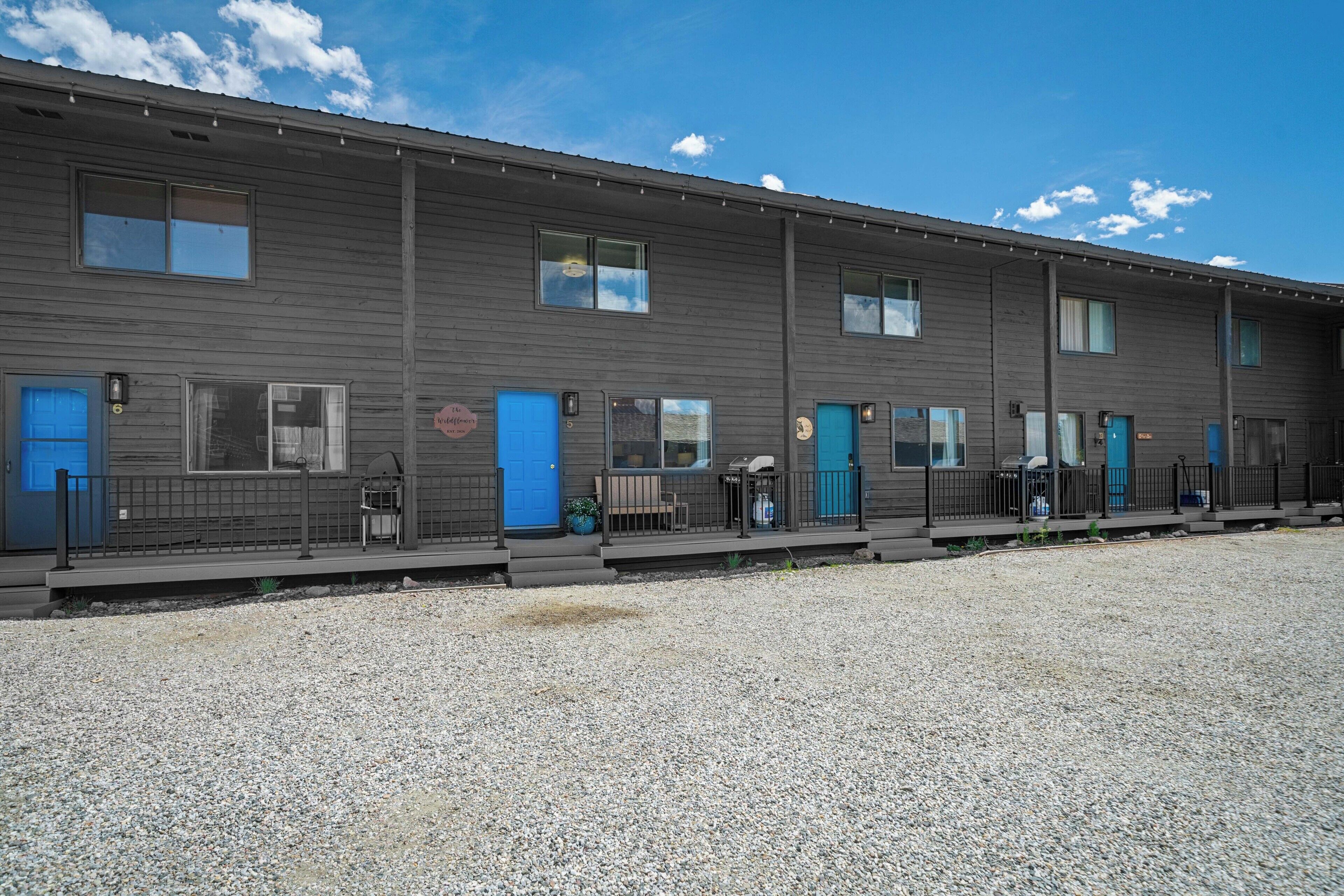 Una hilera de habitaciones de motel con puertas azules, un camino de grava y cielo despejado.