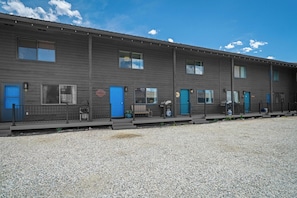 A row of motel rooms with blue doors, a gravel driveway, and a clear sky. - The Wildflower (West Yellowstone)