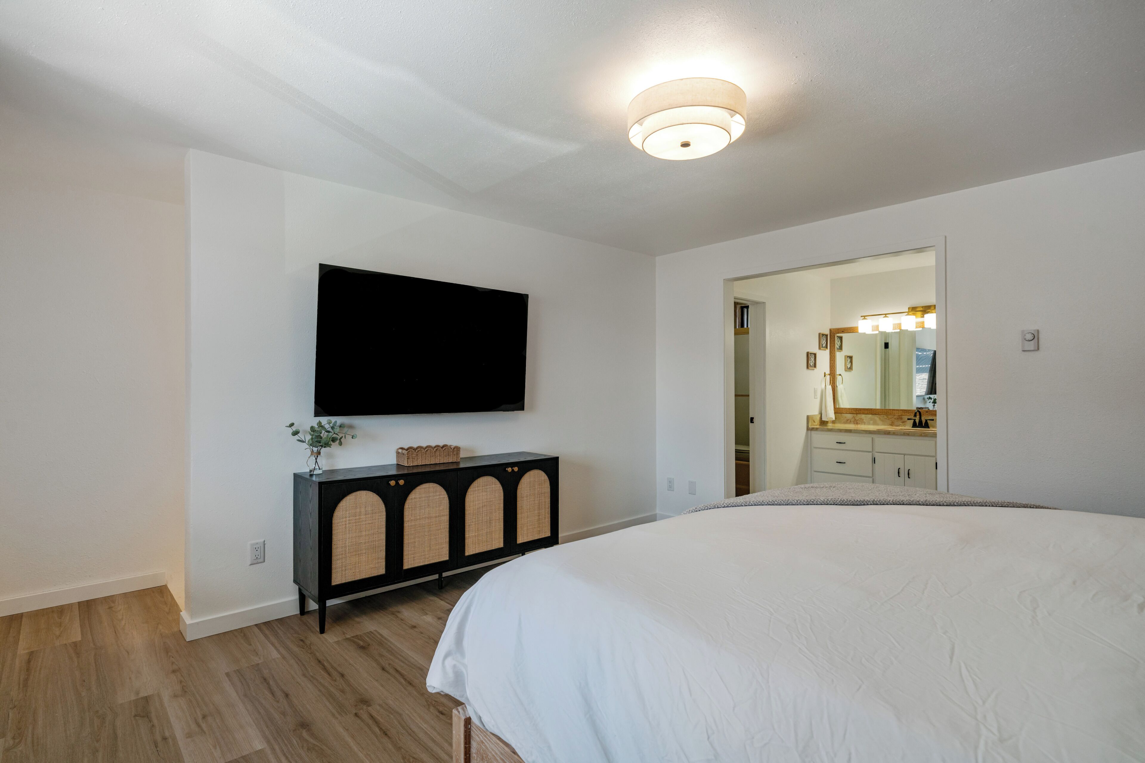 Ein Schlafzimmer mit einem großen Bett, einem flachbildschirmfernseher an der Wand, einer dunklen Holzkommode und einem durch eine offene Tür einsehbaren Badezimmer.