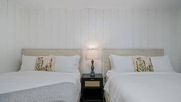 Una habitación con dos camas, una mesita de noche con lámpara y una pared con paneles verticales.
