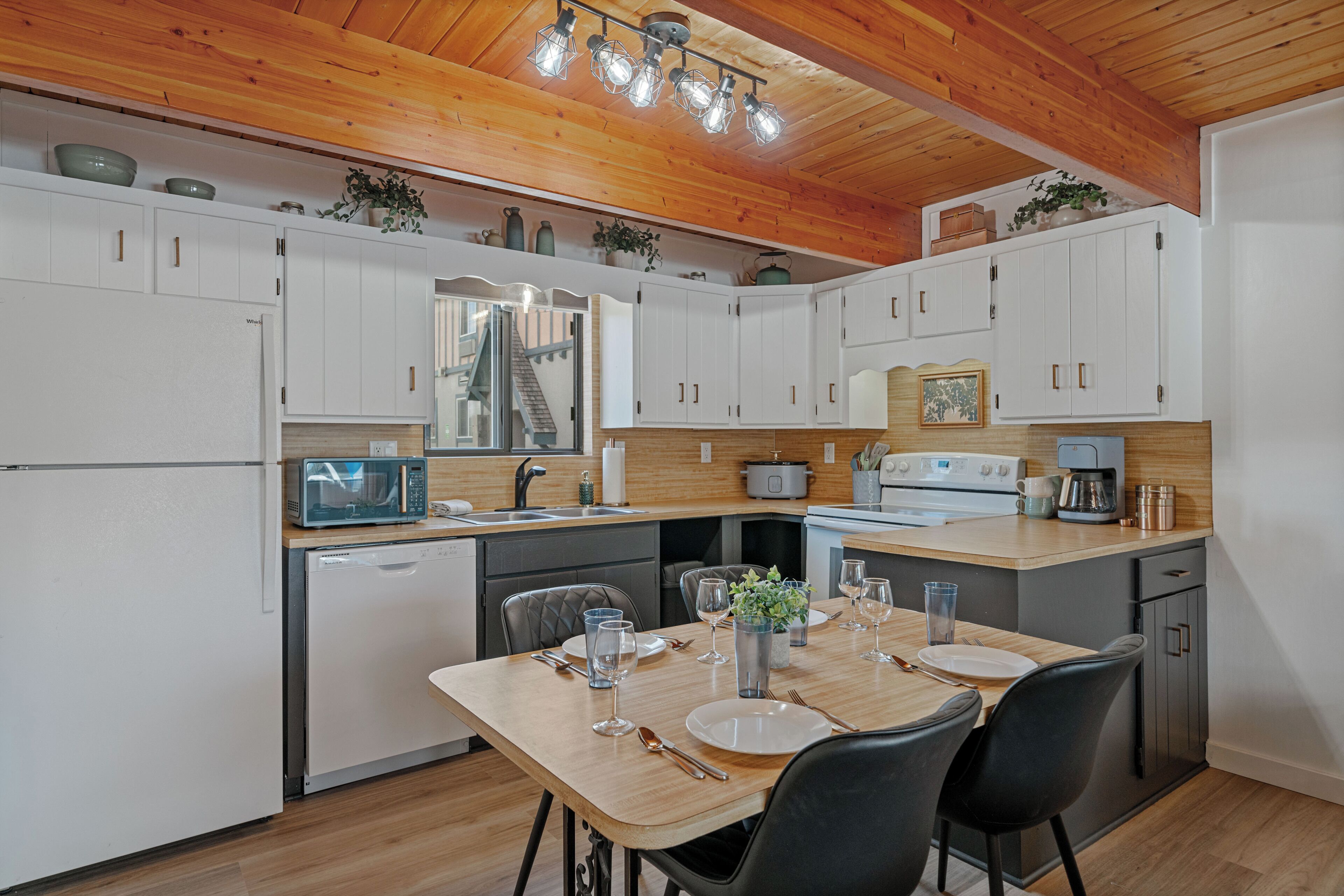 A modern kitchen with white cabinets, a wooden dining table, and a built-in stove.