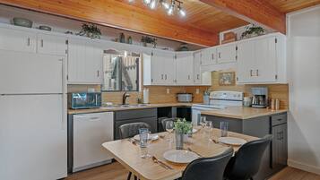 A modern kitchen with white cabinets, a wooden dining table, and a built-in stove.