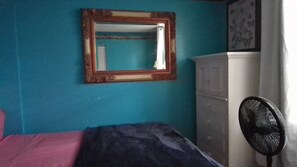 Ein Zimmer mit einem Bett, einem Schrank, einem Spiegel und einem Ventilator.