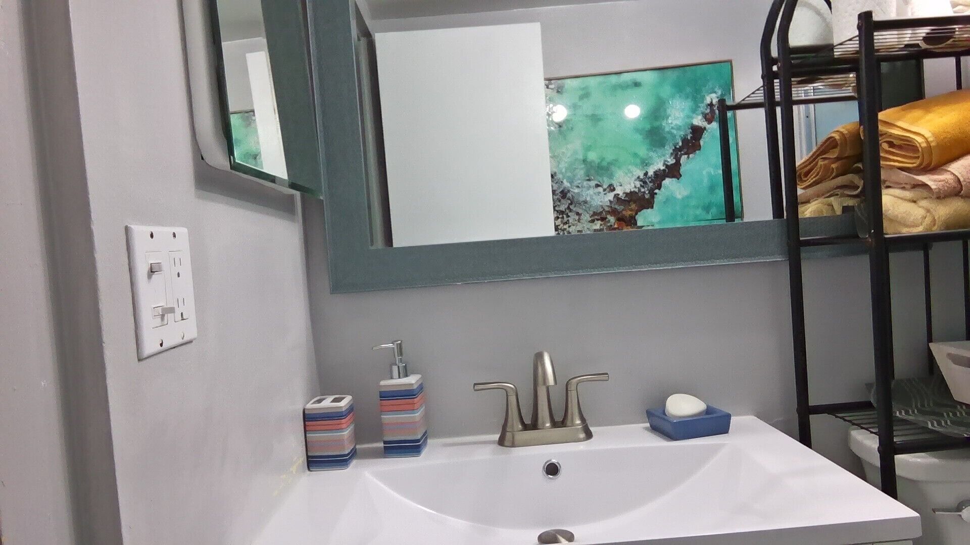 Une salle de bain avec un lavabo blanc, un miroir, un porte-serviettes et une prise électrique.