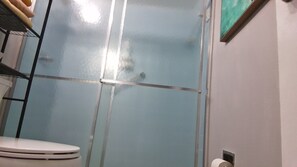 Ein Badezimmer mit Duschkabine aus Glas, Toilette und Handtuchhalter an der Wand.