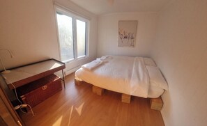 Ein Schlafzimmer mit einem Bett, einem kleinen Schreibtisch, einem Fenster und einem an der Wand hängenden Kunstwerk.