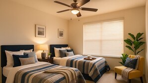 A hotel room with two beds, a ceiling fan, a window with blinds, a chair, and a plant. - Spacious 5-bedroom house in lovely Missouri City with AC (Missouri City)