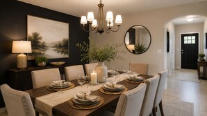 A dining area with a long table set for six, a chandelier, a painting, and a mirror on the wall. - Spacious 5-bedroom house in lovely Missouri City with AC (Missouri City)