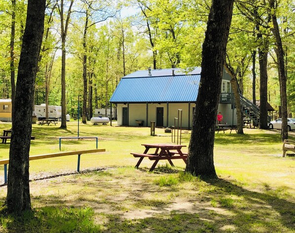 A campsite with picnic tables, a cabin with a blue roof, and surrounding trees.