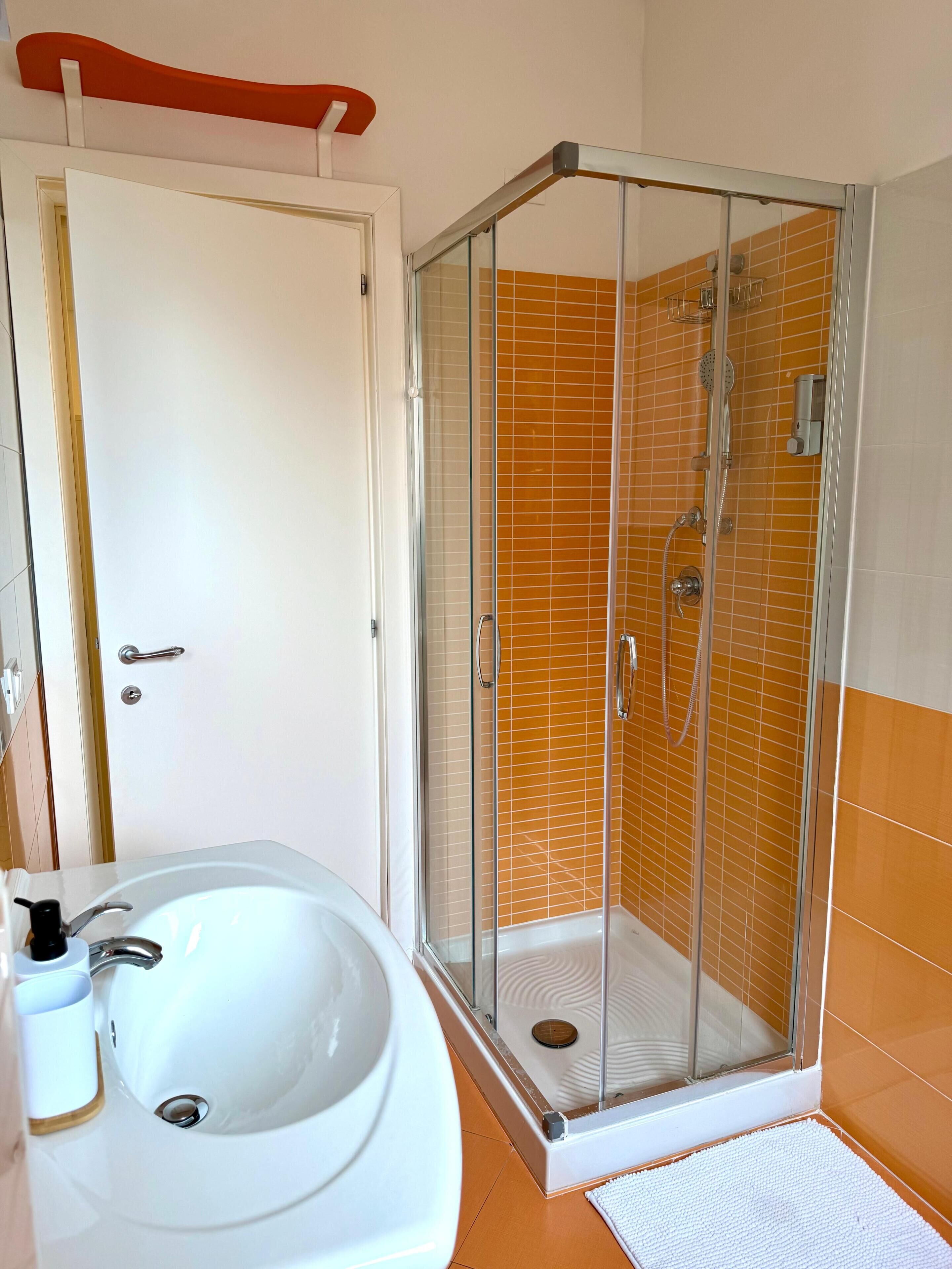 Un baño con ducha envuelta en vidrio, un lavamanos y una puerta.