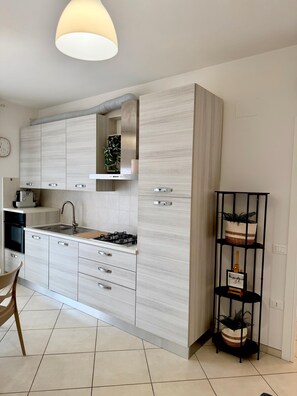 A modern kitchen with light wood cabinetry, a gas stove, a sink, and a dining area with a chair. - Tourist Location Giancola between Seas and Mountains (Bellante Stazione)