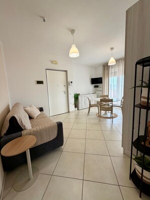 A modern living room with a sofa, a dining table with chairs, a TV mounted on the wall, and a kitchen area in the background. - Tourist Location Giancola between Seas and Mountains (Bellante Stazione)