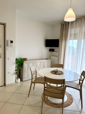 A modern kitchen with a white countertop, a flat-screen TV mounted above it, and a dining area with a round table and chairs. - Tourist Location Giancola between Seas and Mountains (Bellante Stazione)