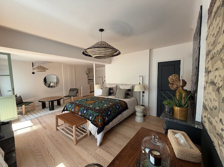 A bedroom with a large bed, a wooden bench, a small table, a floor lamp, and a hanging light fixture.. Luxury B&B room in the center of Chinon