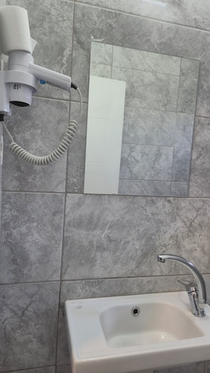 A bathroom with a white sink, a hairdryer, and a mirror. - Aydın ZELİF OTEL  (Efeler)