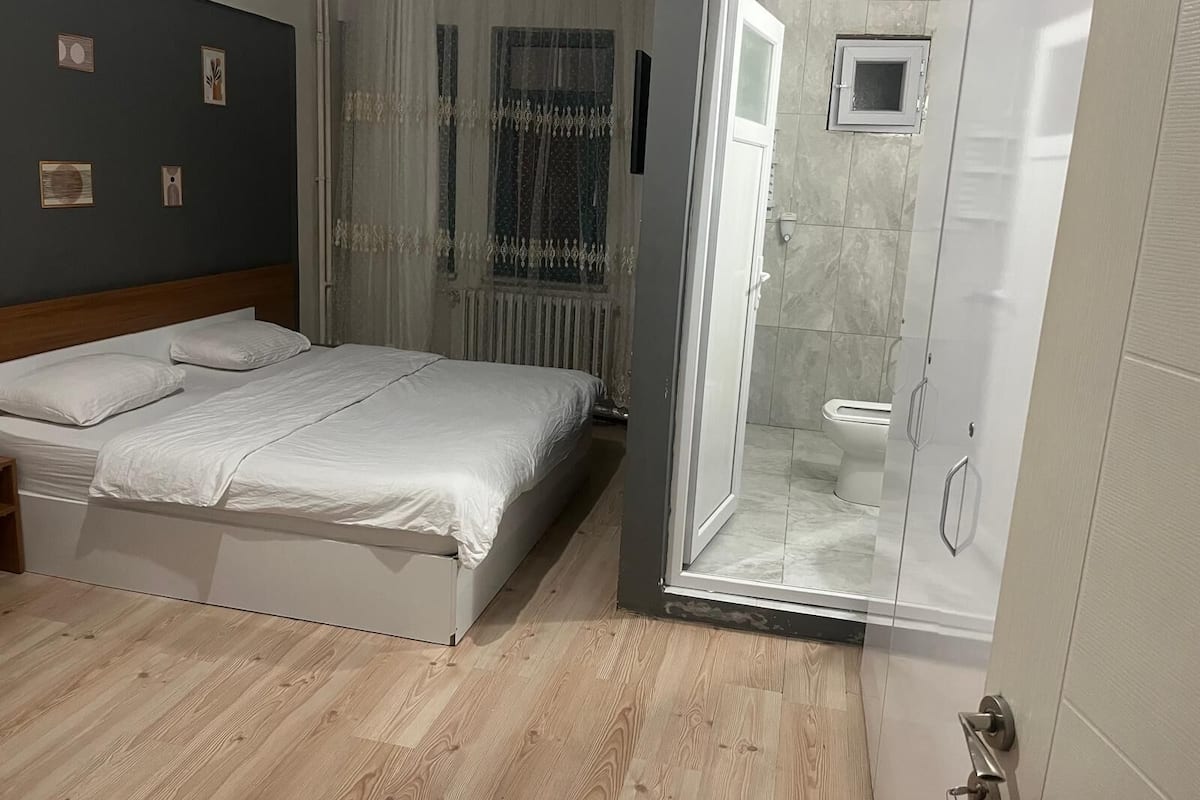 A bedroom with a bed, a shower area, and a window with curtains.