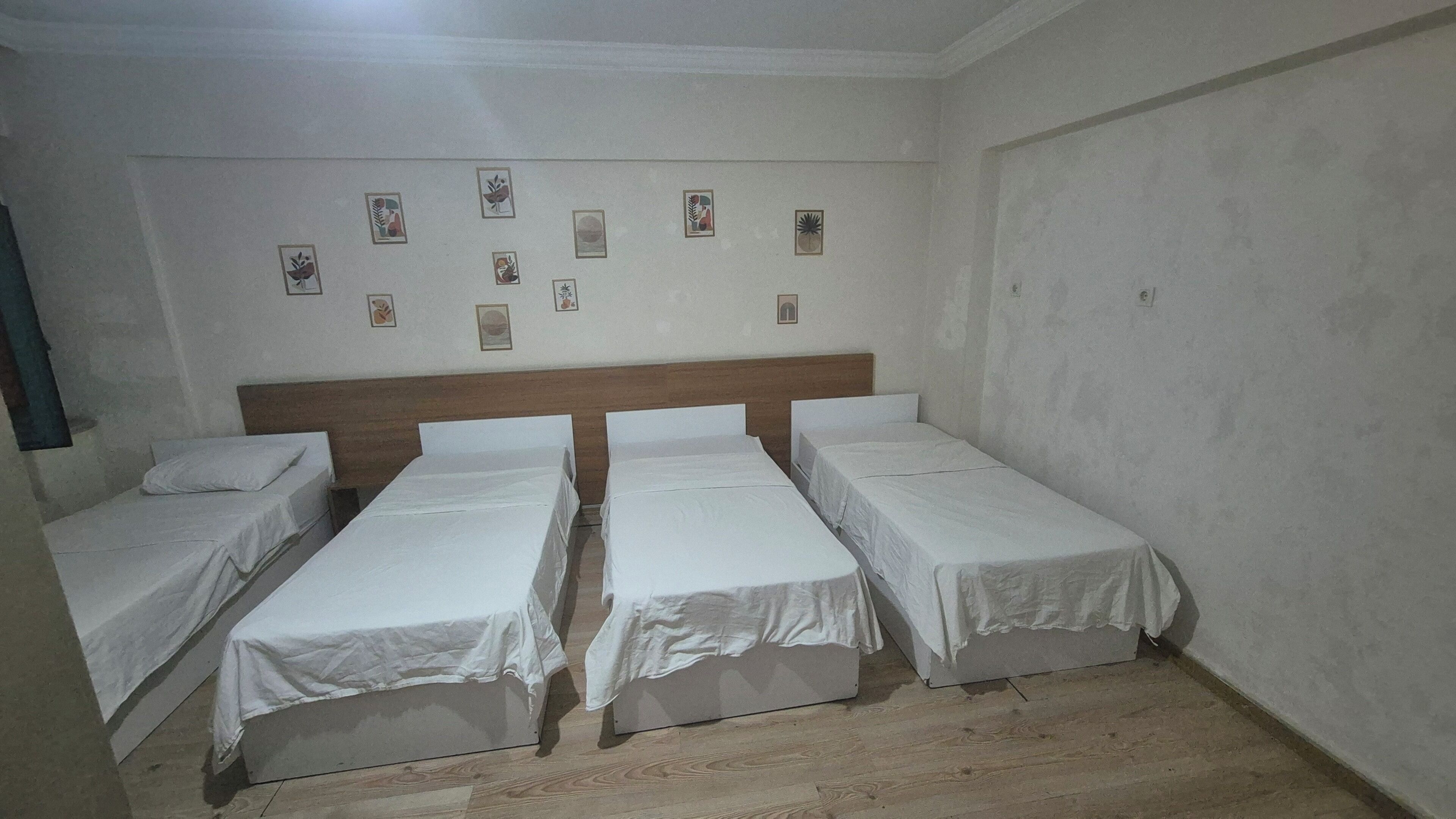 A room with three single beds, a wooden headboard, and a wall decorated with framed pictures.